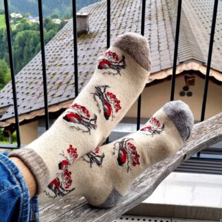 Pieds posés sur du bois portant des chaussettes en laine blanches avec motif cardinal rouge.