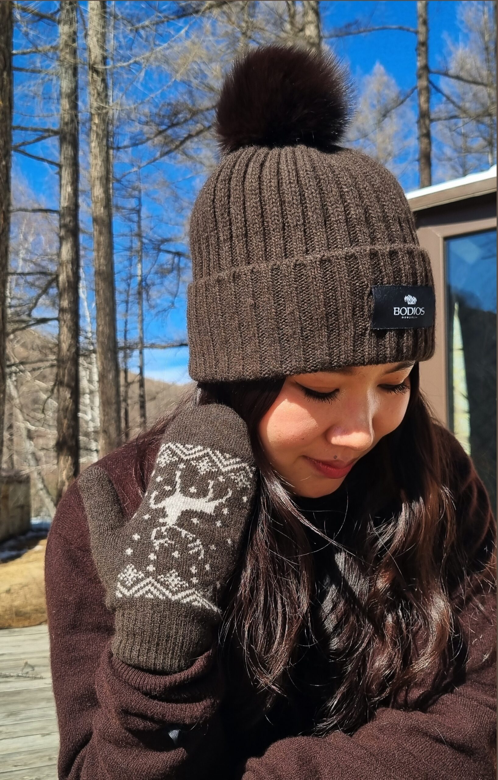 Bonnet à revers en brun chocolat avec pompon et gants à motif jacquard-renne portés sur une jeune femme.